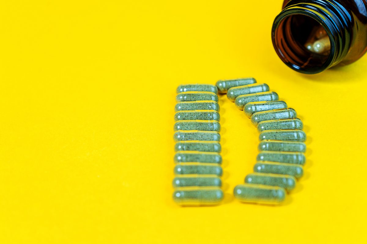 yellow-pills-forming-shape-to-d-alphabet-and-vitamin-d-bottle-on-yellow-background