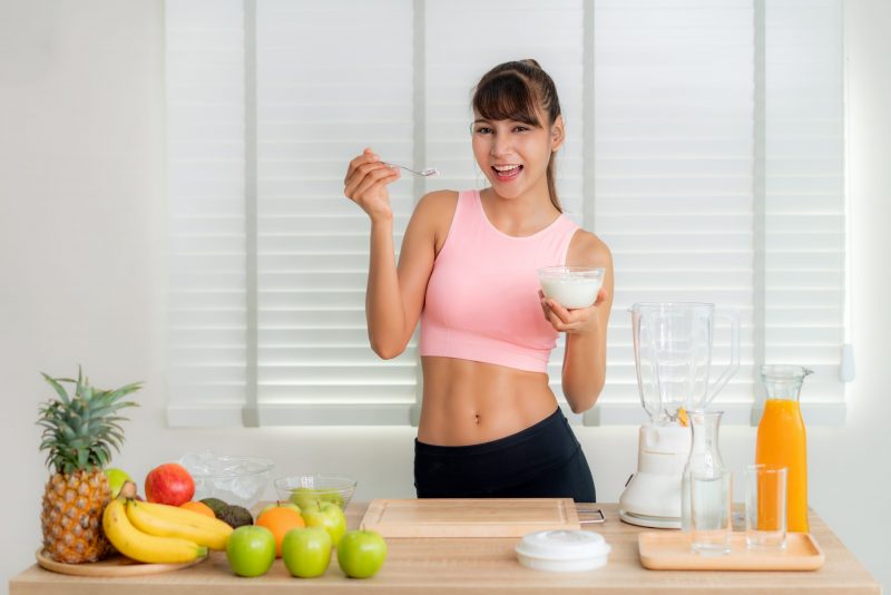 asian-young-woman-wearing-pink-sportware-holding-yogurt-for-squeezing-mix-friut-juice-smoothie-with-appleorange-banana-pineapple-and-avocado-at-kitchen-table-healthy-food-and-diet-lifestyle-for-sl-7