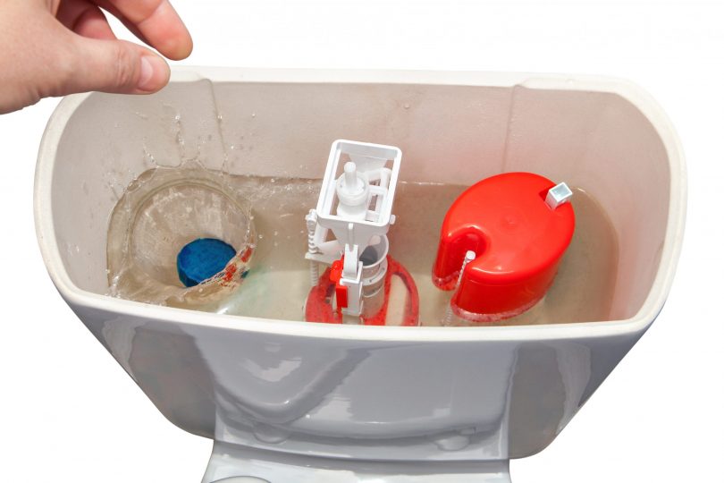 hand-throws-blue-cleaner-tablet-in-flush-tank-toilet-bowl