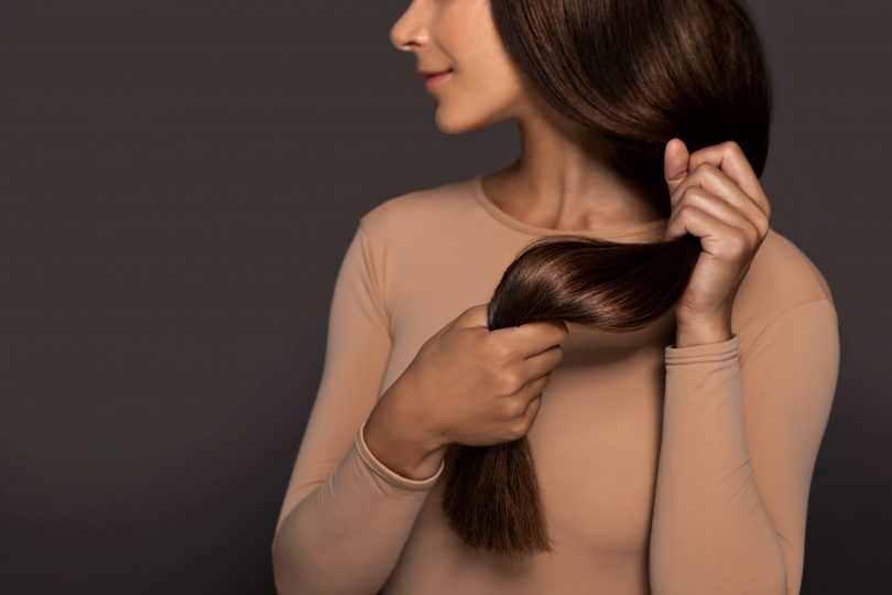 brunette-girl-with-long-straight-and-shiny-hair-beauty-skin-woman-holding-her-strong-and-healthy-hair-in-her-hands-over-grey-background-cosmetic-hair-beauty-salon-concept