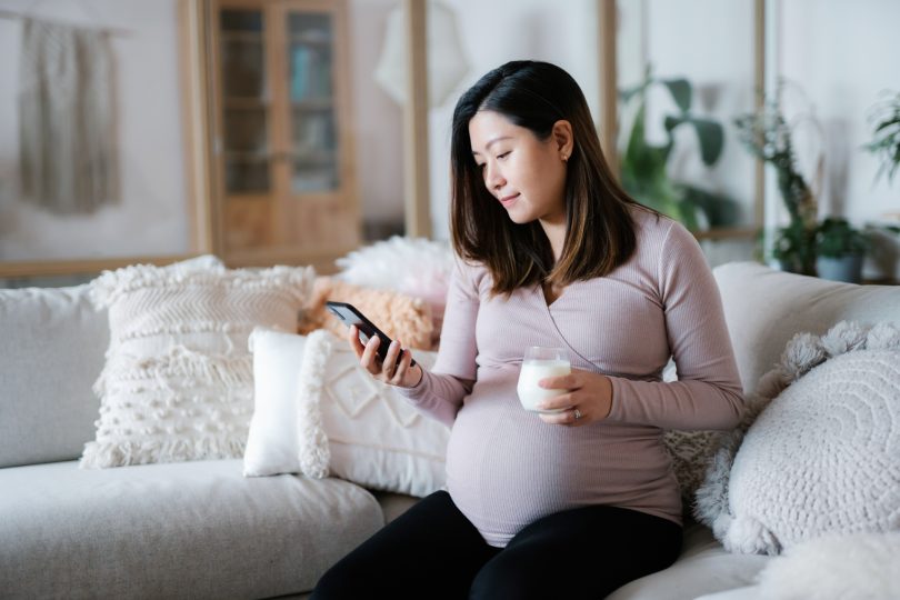 beautiful-young-asian-pregnant-woman-relaxing-on-sofa-in-the-living-room-at-cozy-home-drinking-a-glass-of-fresh-milk-and-using-smartphone-wellbeing-healthy-eating-lifestyle-during-pregnancy