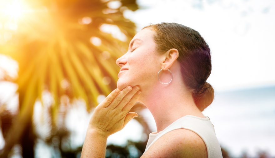 mid-adult-woman-applies-lotion-to-her-face-outdoors-profile