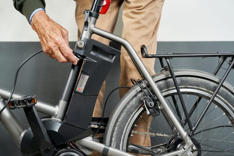 hand-of-caucasian-man-charging-battery-pack-on-electric-bicycle-at-garage-transport-concept